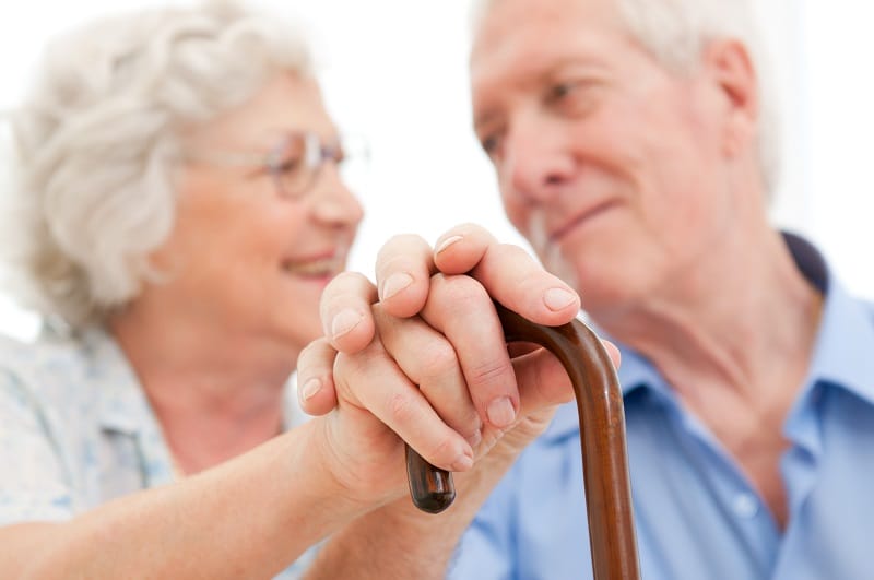 Elderly couple holding hands, one with a walking cane.
