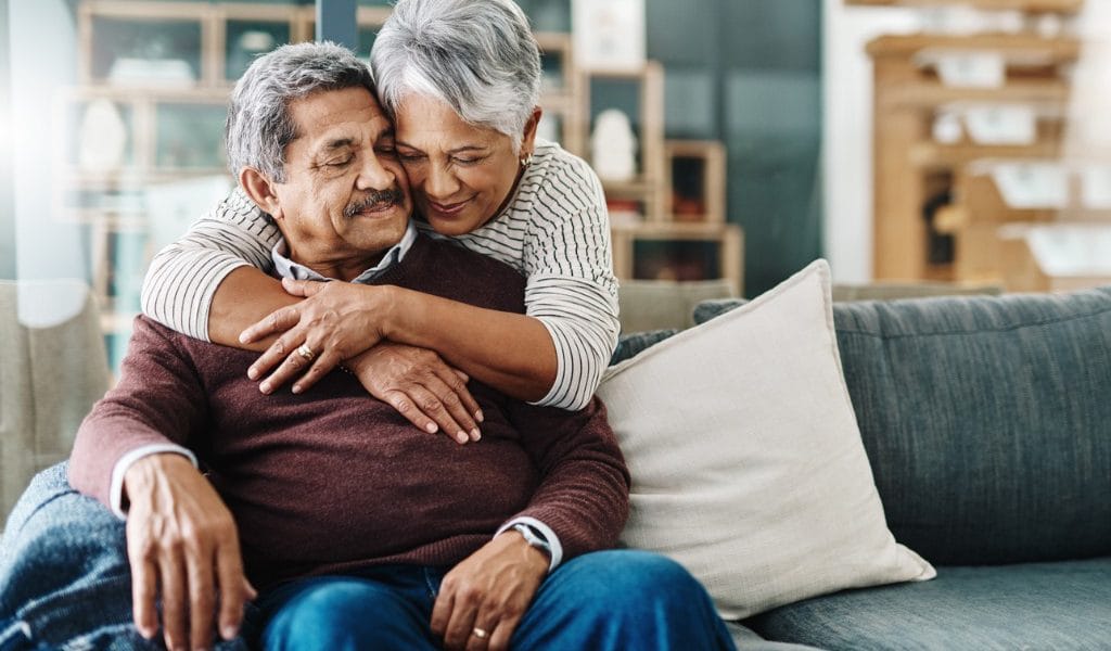 Senior couple sharing a tender embrace on a couch.